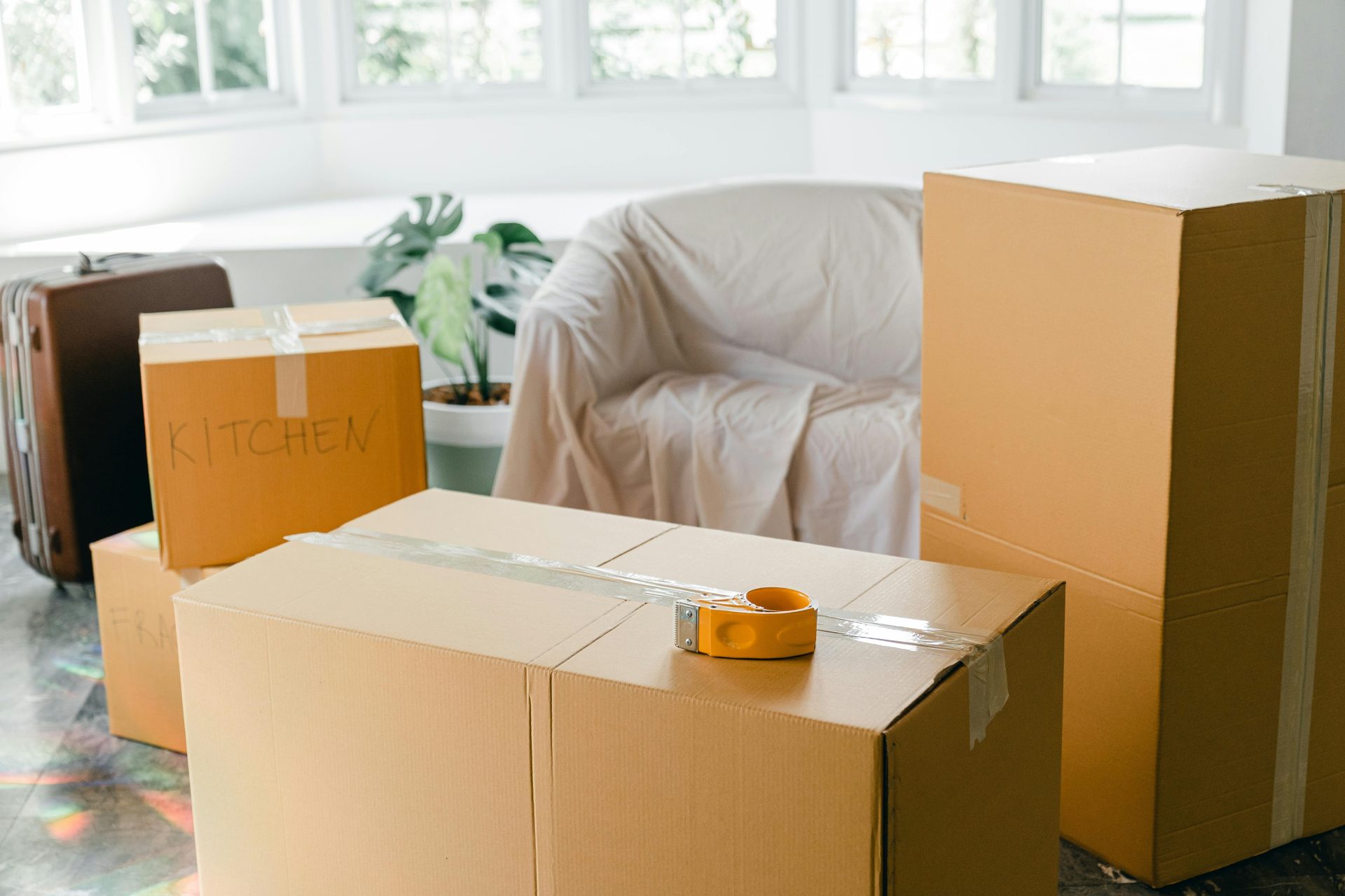 Diverse Kartons mit Haushaltsgegenständen und ein Koffer standen vor dem Umzug in die neue Wohnung in einem hellen Zimmer auf dem Boden.